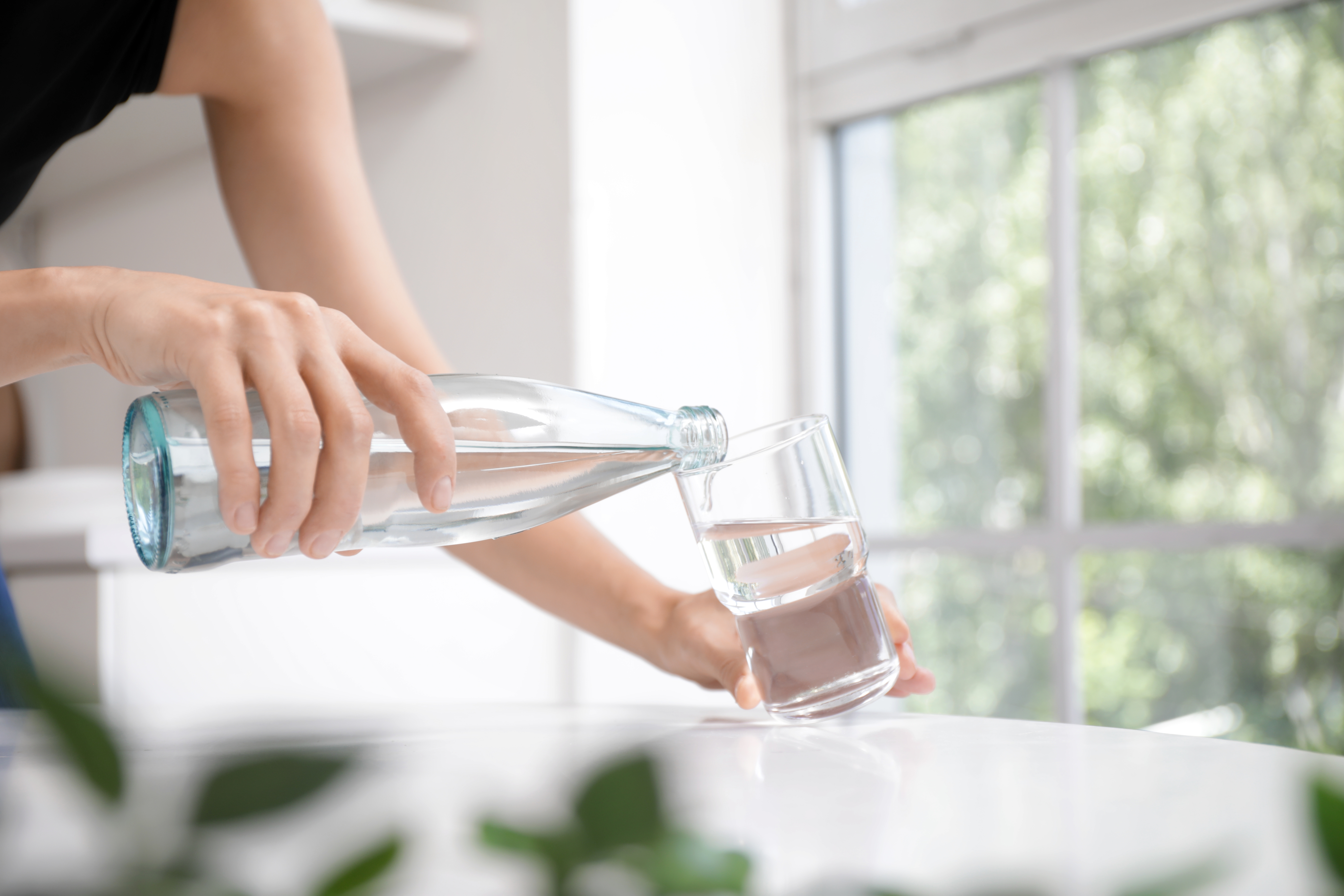 家でボトルからグラスに水を注ぐ女性、接写