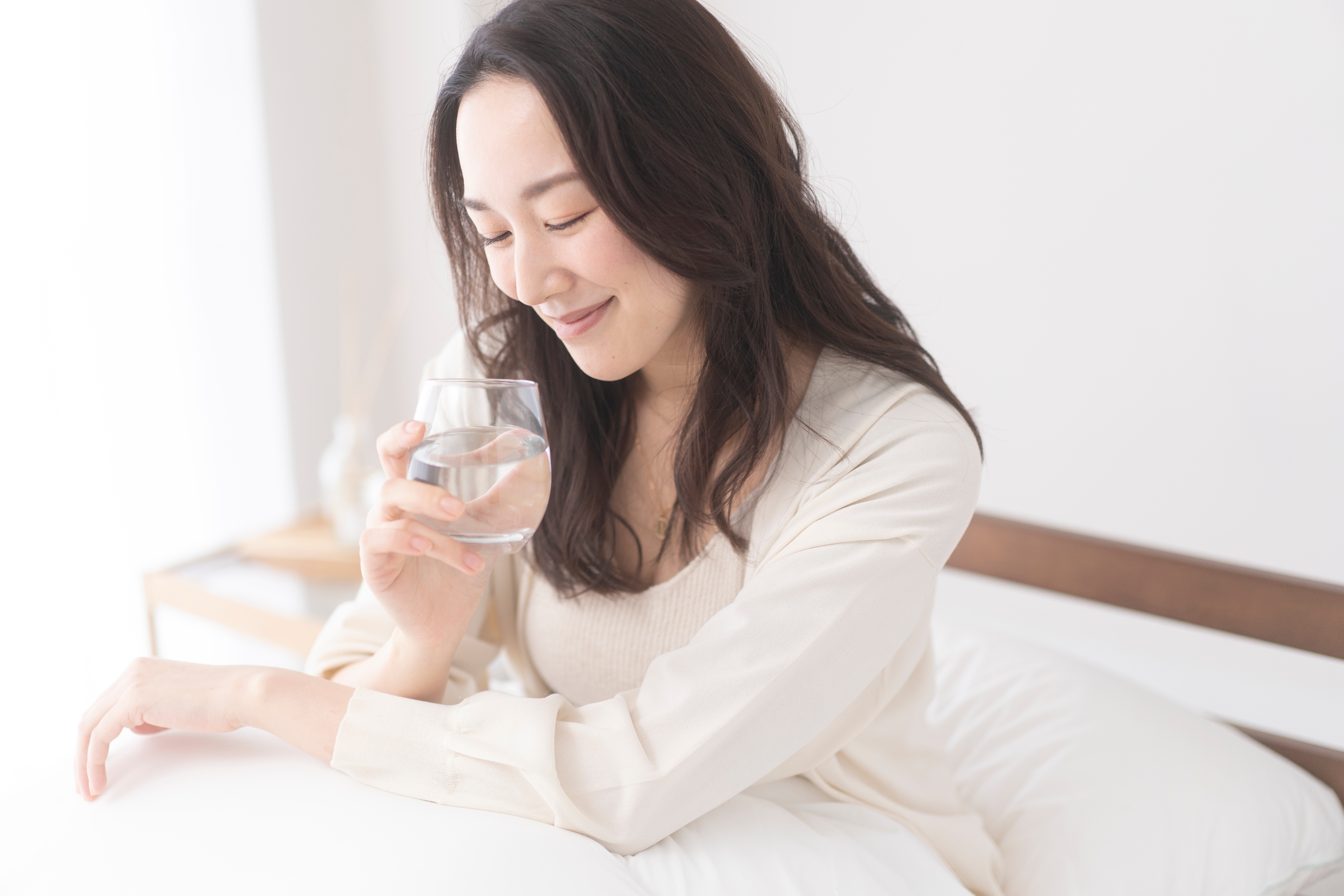 ある中年の女性が朝、ベッドでコップ一杯の水を飲んでいる