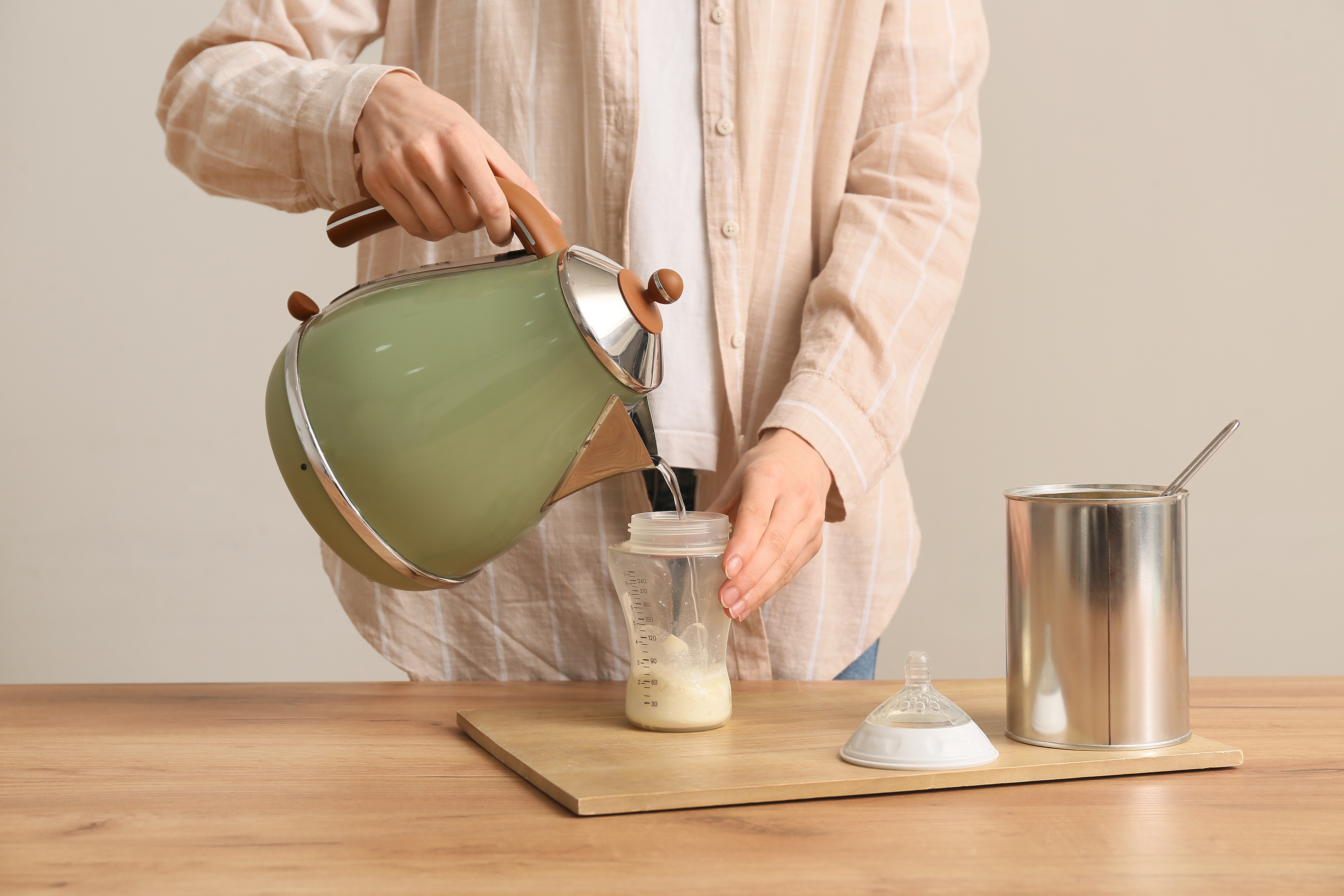 グレイの壁に木のテーブルでベビーミルクの処方を準備する女性